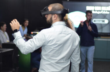 Pessoa utilizando óculos de realidade virtual durante uma apresentação sobre inteligência artificial e inovação tecnológica, enquanto participantes acompanham a demonstração em um ambiente de aprendizagem e tecnologia.