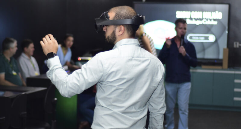 Pessoa utilizando óculos de realidade virtual durante uma apresentação sobre inteligência artificial e inovação tecnológica, enquanto participantes acompanham a demonstração em um ambiente de aprendizagem e tecnologia.