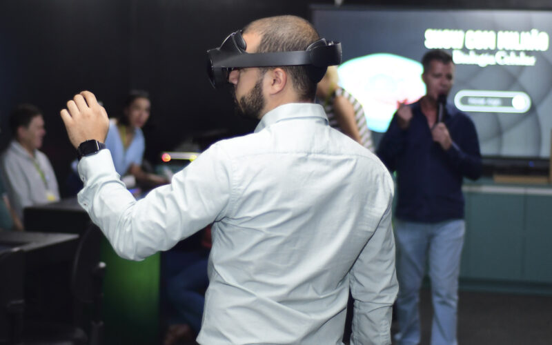 Pessoa utilizando óculos de realidade virtual durante uma apresentação sobre inteligência artificial e inovação tecnológica, enquanto participantes acompanham a demonstração em um ambiente de aprendizagem e tecnologia.