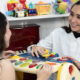 Estudante de Terapia Ocupacional da Unoeste realiza atividade prática utilizando brinquedo educativo em atendimento simulado. A cena ocorre em um ambiente terapêutico com brinquedos, materiais lúdicos e recursos utilizados no desenvolvimento de habilidades cognitivas, motoras e sensoriais.