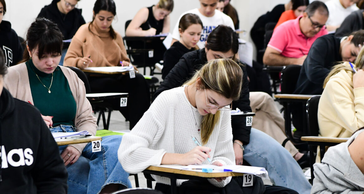 Estudantes universitários realizando prova em sala de aula, sentados em carteiras individuais e concentrados na resolução das questões de uma avaliação acadêmica.