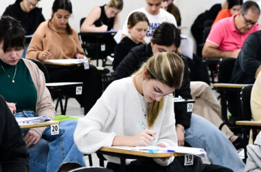 Estudantes universitários realizando prova em sala de aula, sentados em carteiras individuais e concentrados na resolução das questões de uma avaliação acadêmica.