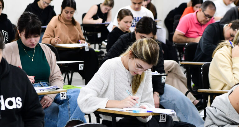 Estudantes universitários realizando prova em sala de aula, sentados em carteiras individuais e concentrados na resolução das questões de uma avaliação acadêmica.