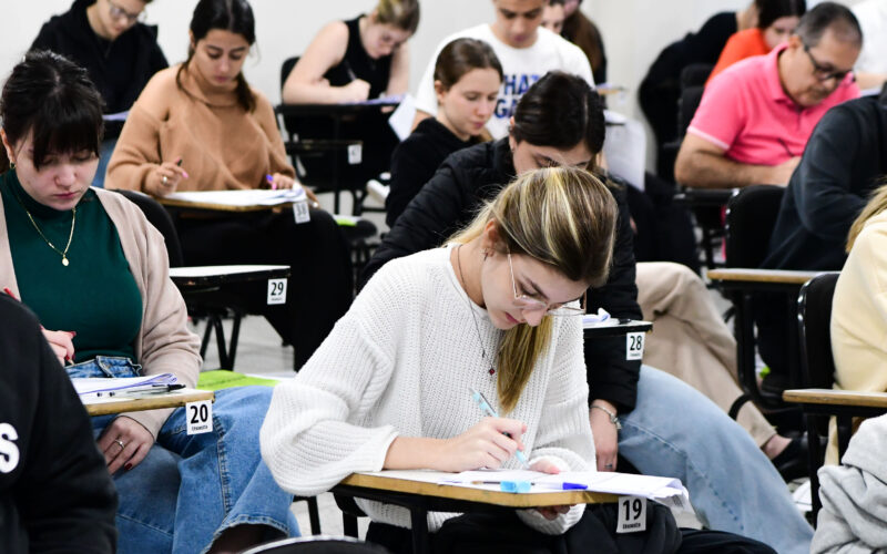 Estudantes universitários realizando prova em sala de aula, sentados em carteiras individuais e concentrados na resolução das questões de uma avaliação acadêmica.