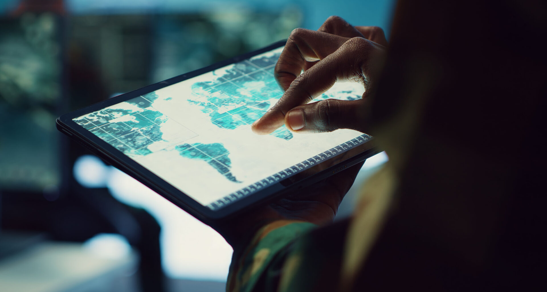 Close-up de uma pessoa utilizando os dedos para navegar em um mapa digital exibido em um tablet. A tela apresenta informações geográficas organizadas em áreas delimitadas, simulando uma análise realizada em um Sistema de Informação Geográfica (SIG), tecnologia utilizada para mapear territórios, analisar dados espaciais e apoiar a tomada de decisões em diferentes setores.