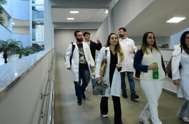 Estudantes de Medicina caminham pelos corredores do campus da Unoeste durante a rotina acadêmica, em ambiente moderno e amplo, que integra espaços de convivência e aprendizagem para a formação médica.