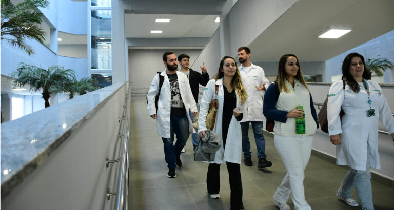 Estudantes de Medicina caminham pelos corredores do campus da Unoeste durante a rotina acadêmica, em ambiente moderno e amplo, que integra espaços de convivência e aprendizagem para a formação médica.