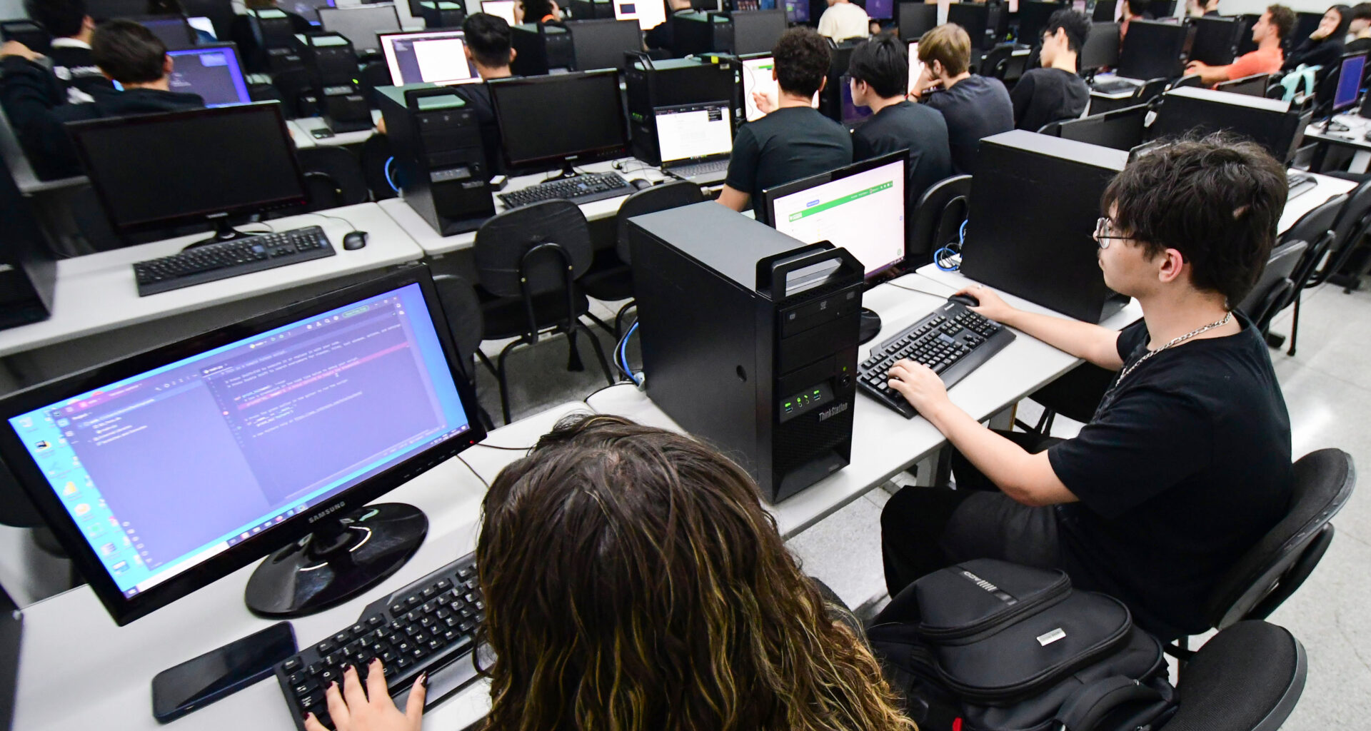 Estudantes utilizam computadores durante aula prática de programação em laboratório de informática, aprendendo linguagens de programação.