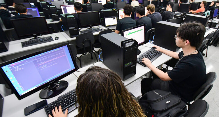 Estudantes utilizam computadores durante aula prática de programação em laboratório de informática, aprendendo linguagens de programação.