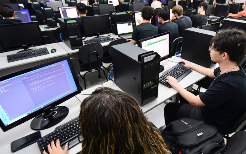 Estudantes utilizam computadores durante aula prática de programação em laboratório de informática, aprendendo linguagens de programação.