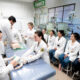 Estudantes de Medicina da Unoeste participam de aula prática em laboratório, com demonstração de procedimento em manequim pediátrico. Ao fundo, o ambiente conta com incubadoras e equipamentos que reproduzem uma unidade neonatal.