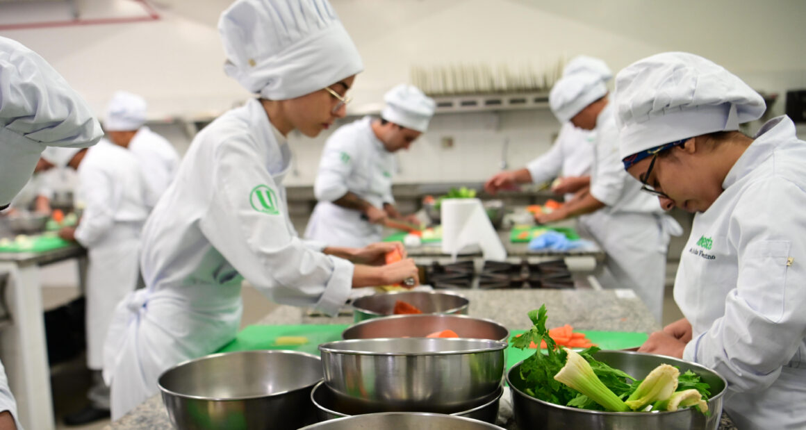 Estudantes da faculdade de Gastronomia da Unoeste participam de uma aula prática em laboratório de cozinha, preparando ingredientes, utilizando utensílios profissionais e desenvolvendo técnicas culinárias essenciais para a formação de futuros chefs de cozinha e personal chefs.