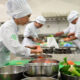 Estudantes da faculdade de Gastronomia da Unoeste participam de uma aula prática em laboratório de cozinha, preparando ingredientes, utilizando utensílios profissionais e desenvolvendo técnicas culinárias essenciais para a formação de futuros chefs de cozinha e personal chefs.