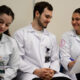 studantes de Medicina da Unoeste, usando jalecos, realizam atividade acadêmica em grupo durante aula prática, registrando informações em pranchetas e discutindo casos clínicos em ambiente de aprendizagem colaborativa.