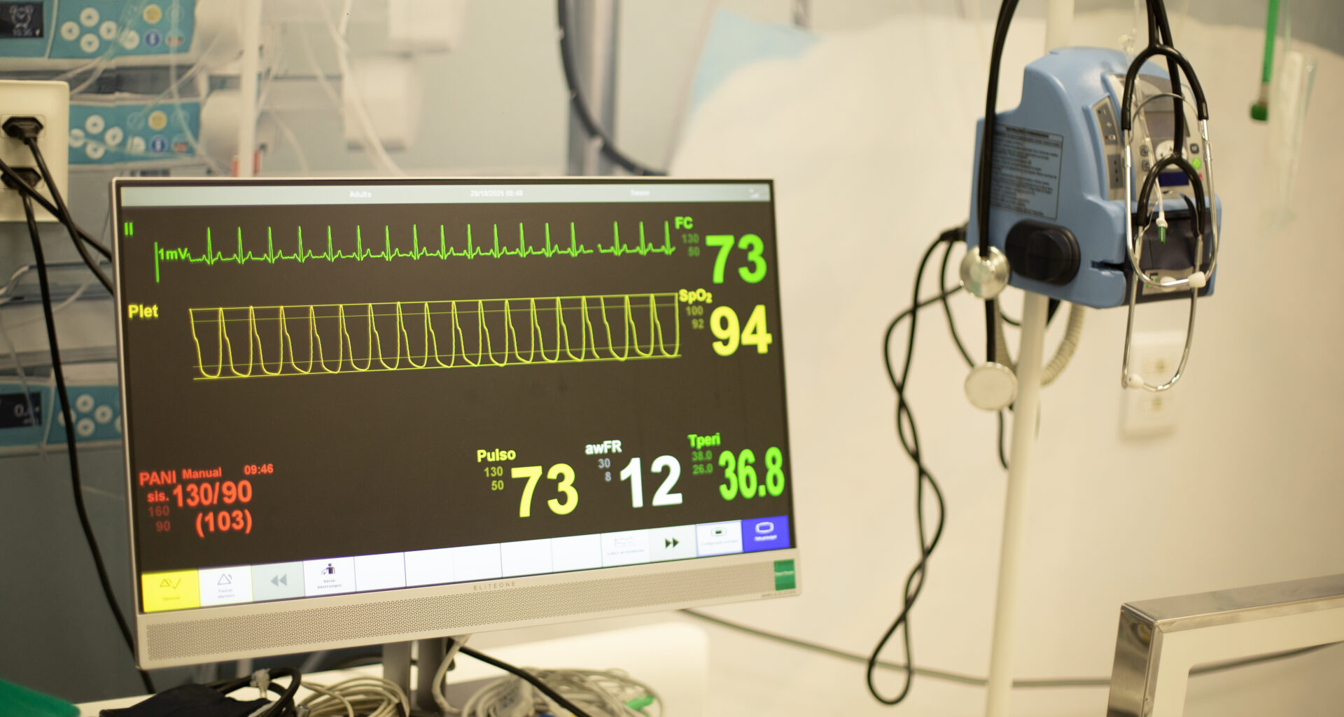 Monitor multiparamétrico exibe frequência cardíaca, pressão arterial, saturação de oxigênio e outros sinais vitais em ambiente de prática médica.