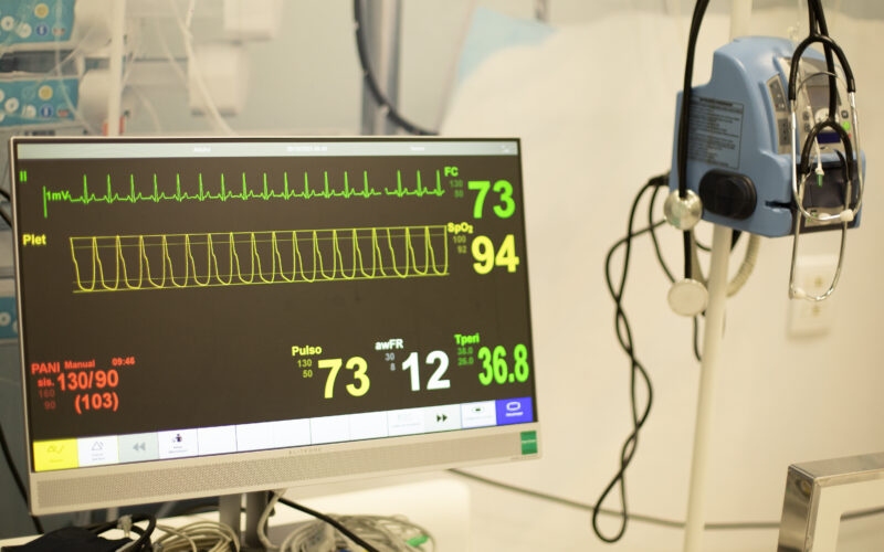Monitor multiparamétrico exibe frequência cardíaca, pressão arterial, saturação de oxigênio e outros sinais vitais em ambiente de prática médica.
