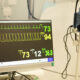 Monitor multiparamétrico exibe frequência cardíaca, pressão arterial, saturação de oxigênio e outros sinais vitais em ambiente de prática médica.
