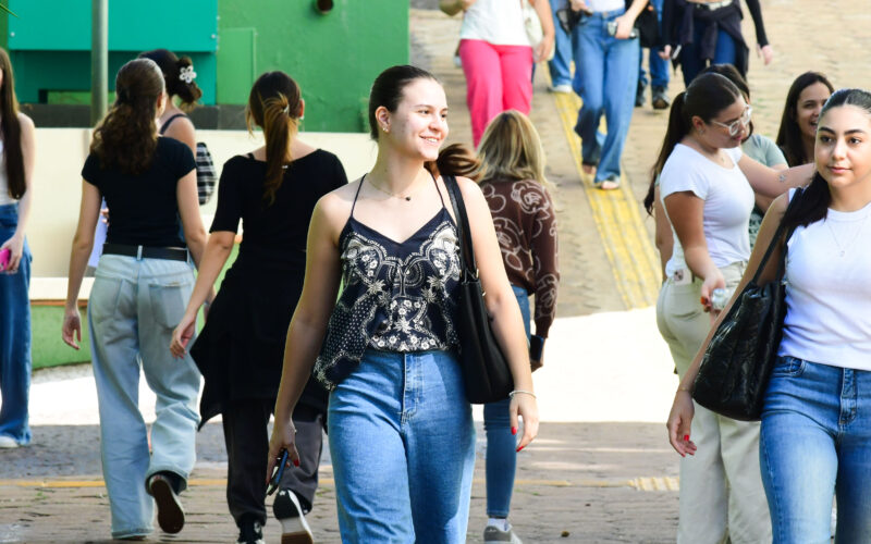 Alunos circulam pelo campus da Unoeste durante o intervalo das aulas, carregando mochilas e bolsas em um ambiente universitário.