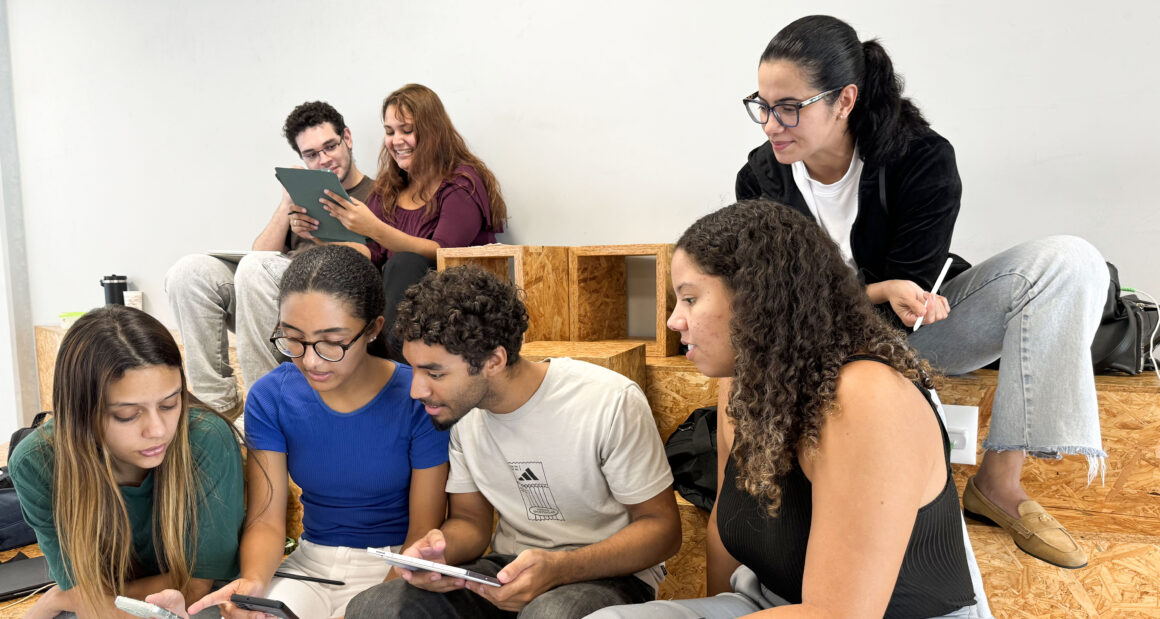 Estudantes da Unoeste reunidos em um espaço de convivência, utilizando celulares e tablets enquanto conversam e realizam uma atividade acadêmica em grupo.