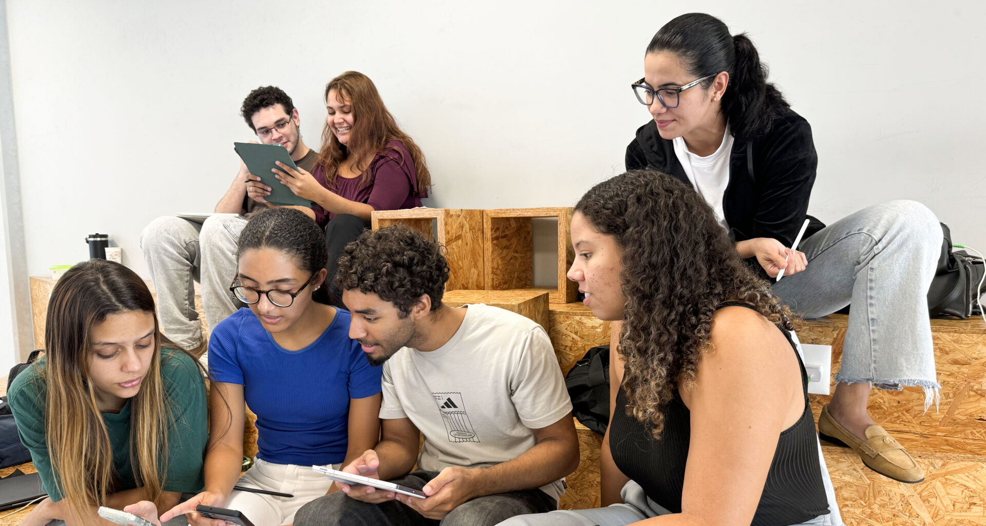 Estudantes da Unoeste reunidos em um espaço de convivência, utilizando celulares e tablets enquanto conversam e realizam uma atividade acadêmica em grupo.