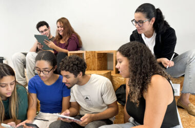 Estudantes da Unoeste reunidos em um espaço de convivência, utilizando celulares e tablets enquanto conversam e realizam uma atividade acadêmica em grupo.