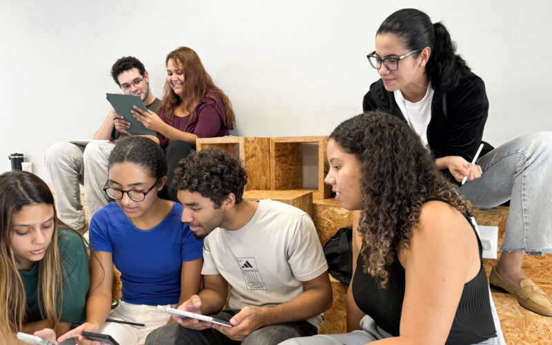 Estudantes da Unoeste reunidos em um espaço de convivência, utilizando celulares e tablets enquanto conversam e realizam uma atividade acadêmica em grupo.