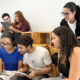 Estudantes da Unoeste reunidos em um espaço de convivência, utilizando celulares e tablets enquanto conversam e realizam uma atividade acadêmica em grupo.