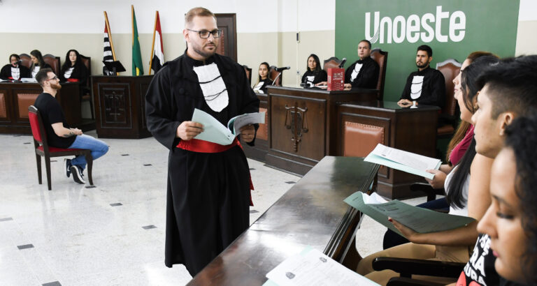 Estudantes do curso de Direito participam de atividade prática em tribunal simulado da Unoeste, com apresentação diante da bancada de julgamento.