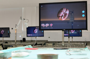 Laboratório de Medicina da Unoeste com telas digitais exibindo modelo 3D do cérebro humano e bancadas com instrumentos utilizados em atividades práticas.