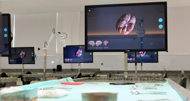 Laboratório de Medicina da Unoeste com telas digitais exibindo modelo 3D do cérebro humano e bancadas com instrumentos utilizados em atividades práticas.