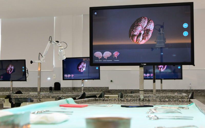 Laboratório de Medicina da Unoeste com telas digitais exibindo modelo 3D do cérebro humano e bancadas com instrumentos utilizados em atividades práticas.