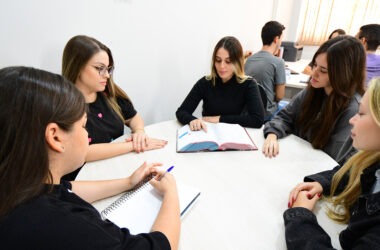 Estudantes do curso de Direito reunidas em uma mesa, estudando e discutindo conteúdos jurídicos com livro e caderno abertos.