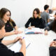 Estudantes do curso de Direito reunidas em uma mesa, estudando e discutindo conteúdos jurídicos com livro e caderno abertos.