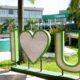 Campus da Unoeste em Presidente Prudente, com letreiro verde e branco “I love U” em primeiro plano, cercado por palmeiras, jardins e área de convivência. Ao fundo, aparece o prédio da universidade com a identificação Unoeste na fachada.