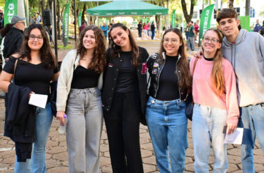 Grupo de jovens posa para foto durante o Vestibular da Unoeste, em área externa do campus decorada com bandeiras verdes da universidade.