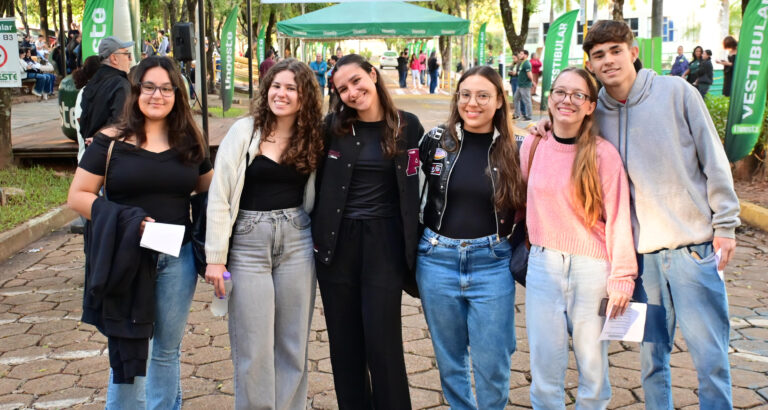 Grupo de jovens posa para foto durante o Vestibular da Unoeste, em área externa do campus decorada com bandeiras verdes da universidade.