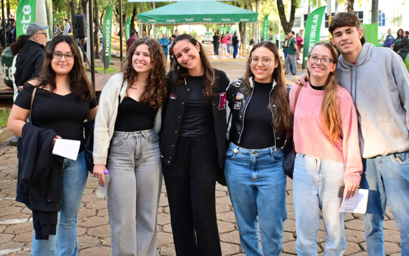 Grupo de jovens posa para foto durante o Vestibular da Unoeste, em área externa do campus decorada com bandeiras verdes da universidade.