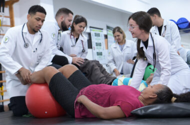 Estudantes de Fisioterapia realizam atendimento prático com pacientes em laboratório, utilizando bola terapêutica durante exercícios de reabilitação.