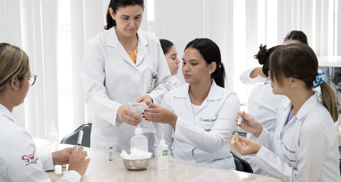 Professora orienta estudantes de Enfermagem da Unoeste durante aula prática com seringas e materiais utilizados em procedimentos de saúde.
