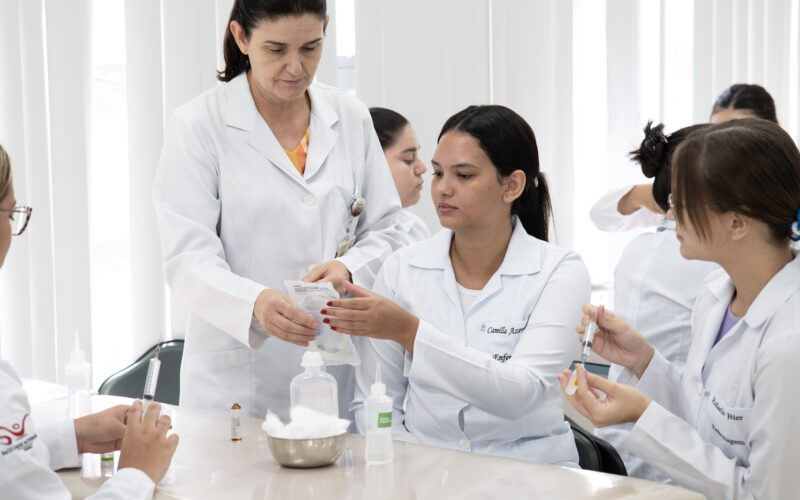 Professora orienta estudantes de Enfermagem da Unoeste durante aula prática com seringas e materiais utilizados em procedimentos de saúde.