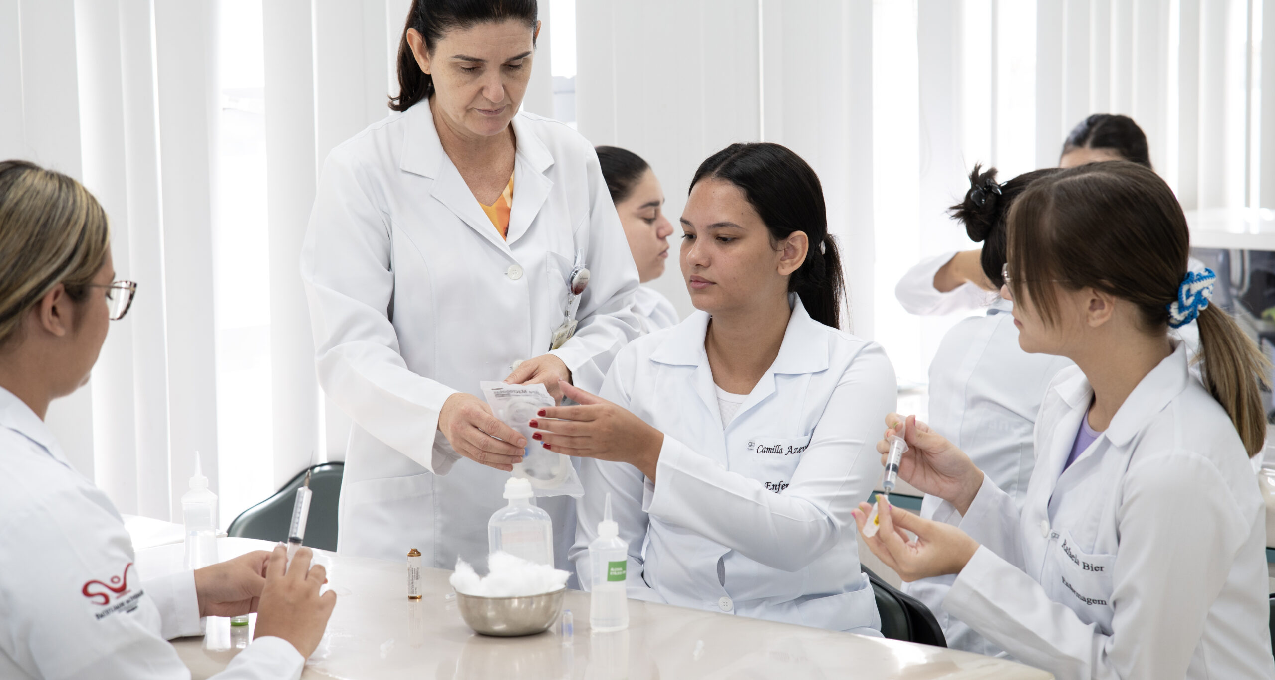 Professora orienta estudantes de Enfermagem da Unoeste durante aula prática com seringas e materiais utilizados em procedimentos de saúde.