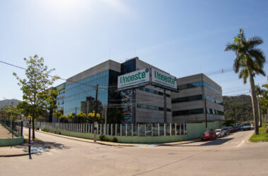 Vista externa do campus da Unoeste em Guarujá, com fachada de vidro e concreto, placas com o nome da universidade e palmeiras ao redor.