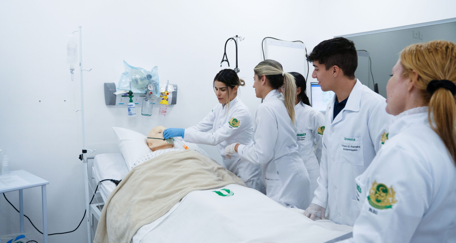 Estudantes de Enfermagem da Unoeste participam de atividade prática em laboratório de simulação, realizando procedimentos em um manequim hospitalar.