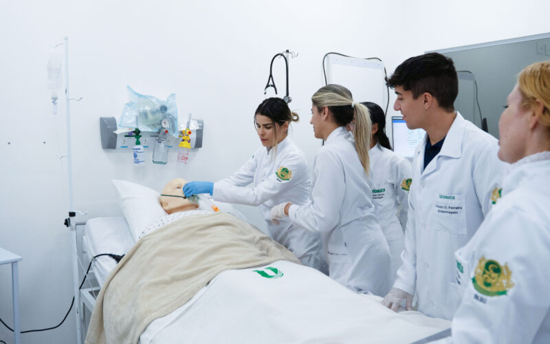 Estudantes de Enfermagem da Unoeste participam de atividade prática em laboratório de simulação, realizando procedimentos em um manequim hospitalar.