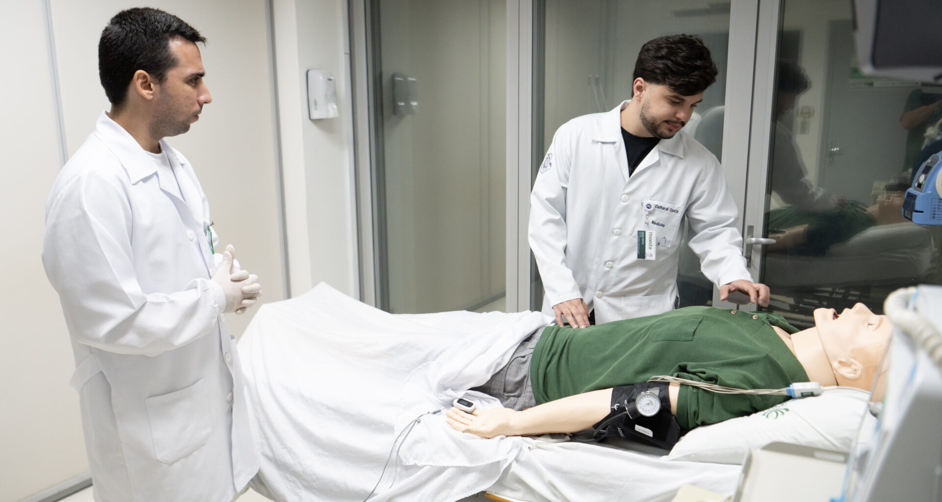 Estudante e professor de Medicina da Unoeste, vestidos com jalecos, realizam treinamento prático com simulador de paciente em laboratório de simulação clínica.