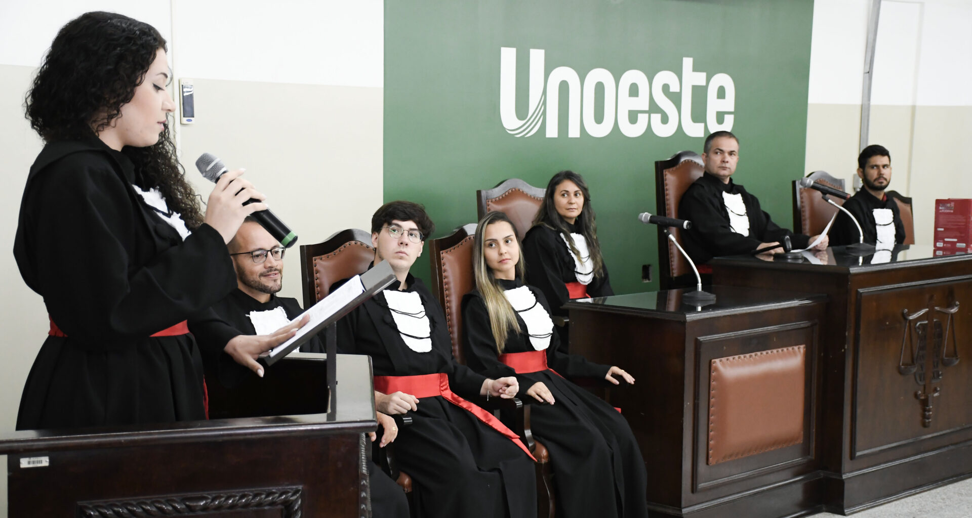Estudantes do curso de Direito da Unoeste participam de atividade prática em tribunal simulado, com apresentação oral diante de uma bancada.