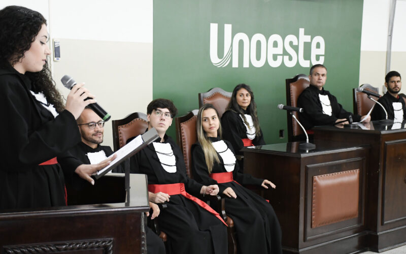 Estudantes do curso de Direito da Unoeste participam de atividade prática em tribunal simulado, com apresentação oral diante de uma bancada.