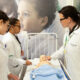 Estudantes de Enfermagem da Unoeste participam de aula prática com professora, realizando simulação de cuidados com um manequim de bebê em laboratório.
