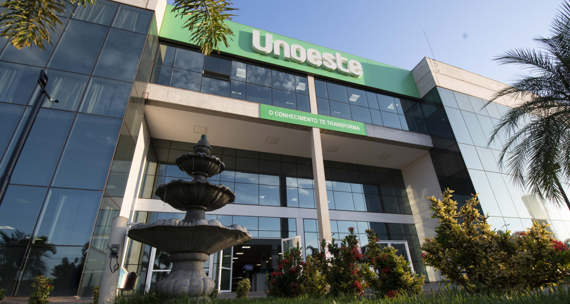 Fachada do campus da Unoeste em Jaú, com entrada principal, fonte e jardins em frente ao prédio da universidade.