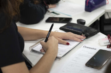 Estudante faz anotações em caderno durante atividade em sala de aula, com materiais da Unoeste sobre a mesa.